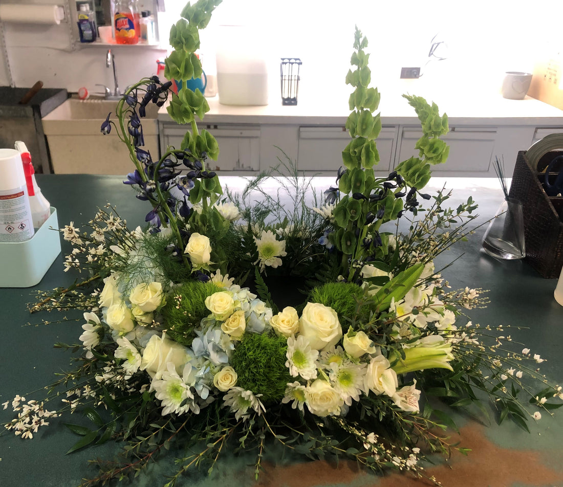 A white and yellow floral urn wreath designed using UrnTray sets on a green table cloth against a white backdrop.