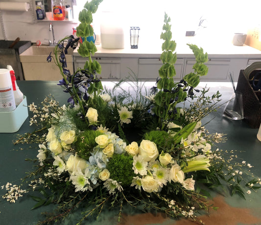 A white and yellow floral urn wreath designed using UrnTray sets on a green table cloth against a white backdrop.