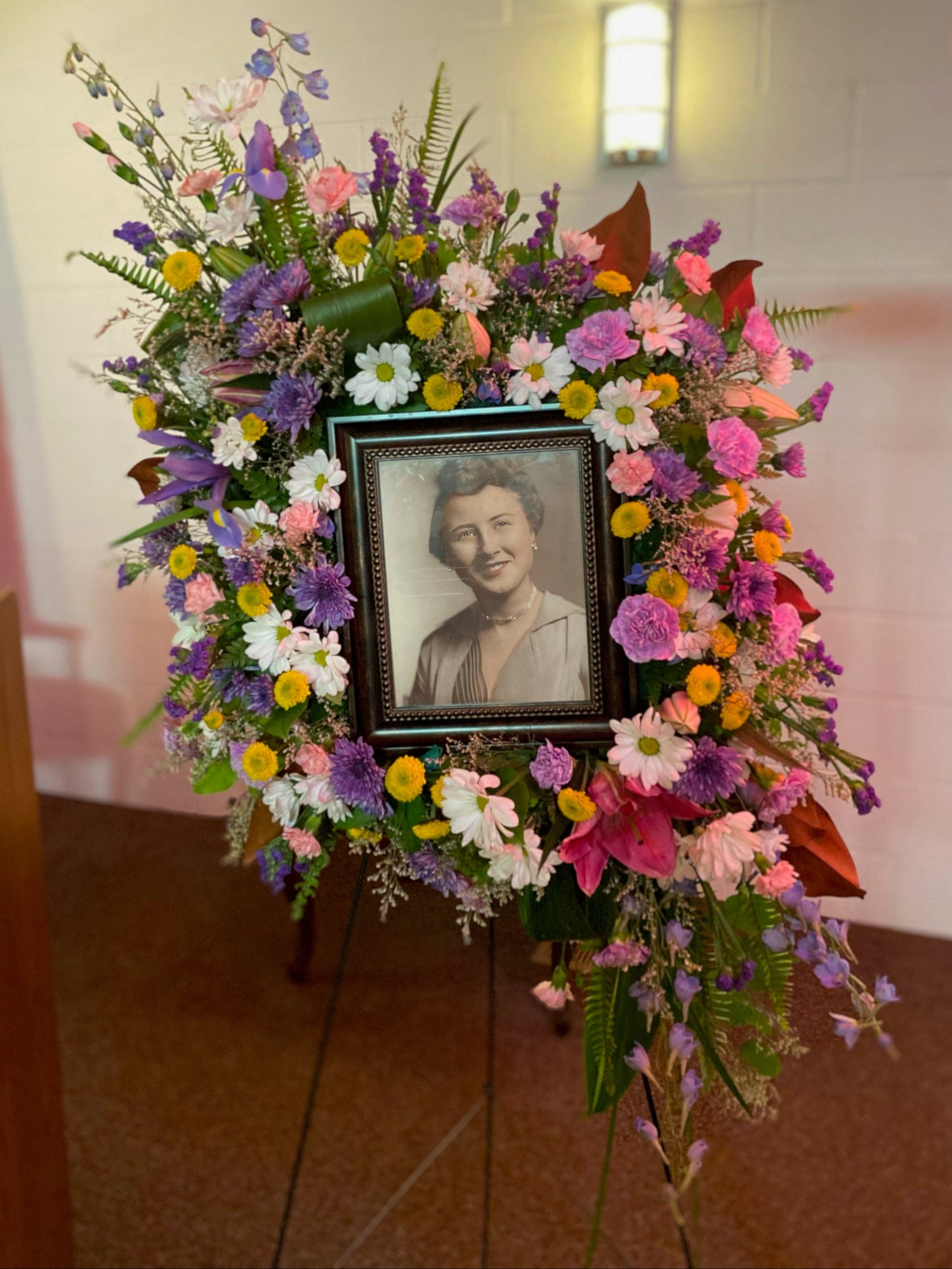 Floral wreath designed using an UrnTray with a photo of a woman in the center, set against a neutral indoor background.