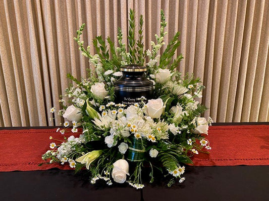A black urn sits in a white-flowered urn wreath designed in an UrnTray