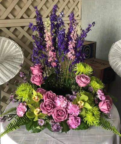 A beautiful urn wreath with roses, mums, and larkspur in shades of purple, pink, and green is designed using an Urn Tray. 